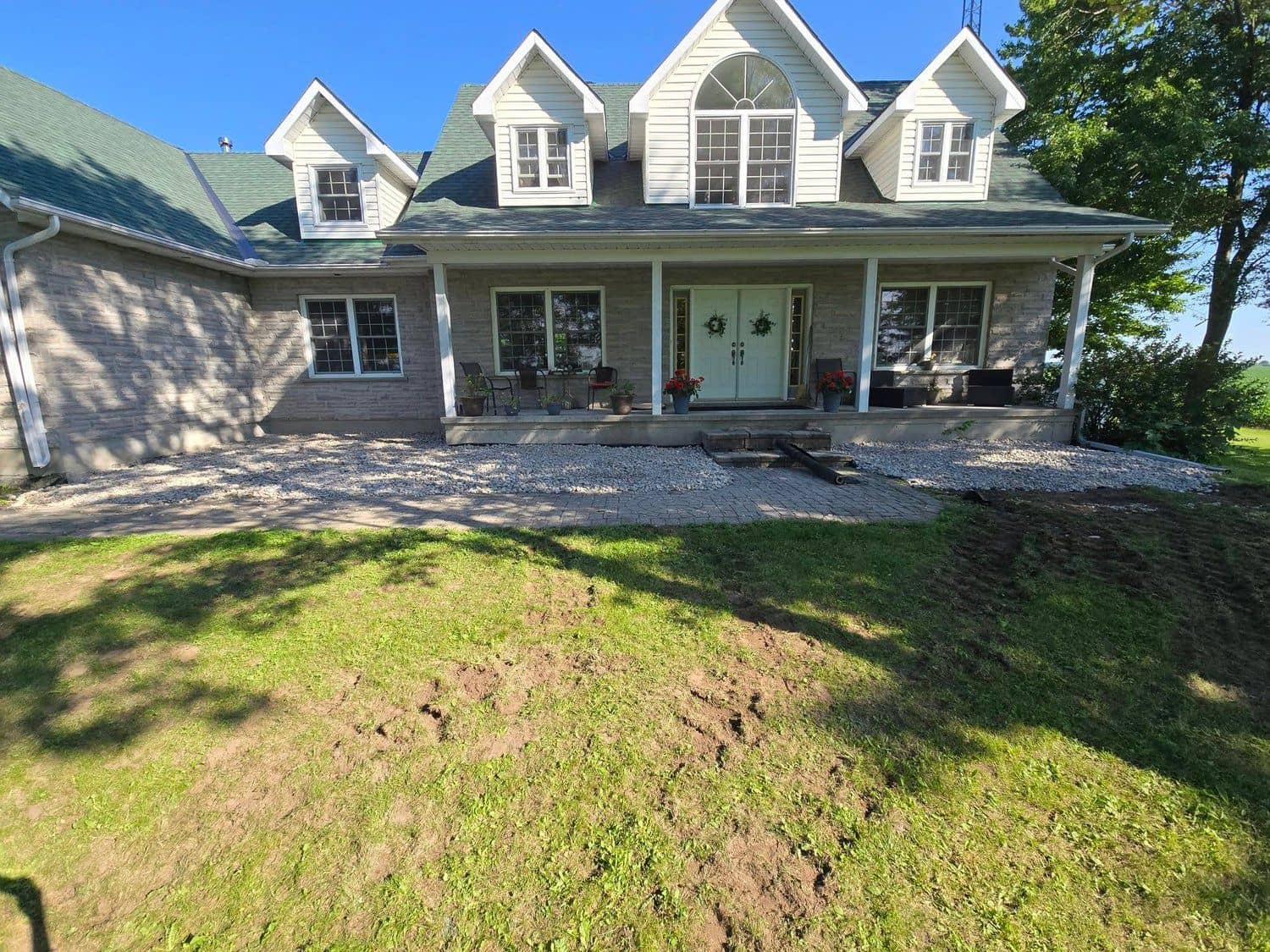 Stone farmhouse in Eastern Ontario with fresh river-rock beds and interlock walkway installed by Home Pride Landscaping