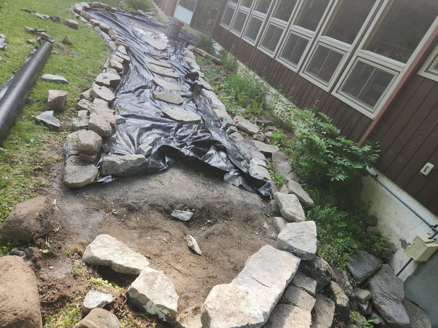 Stone-edged drainage bed with landscape fabric alongside a home
