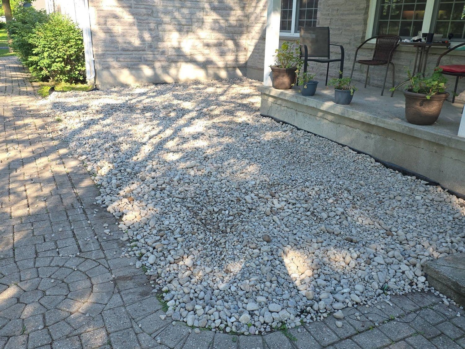 River-rock bed wrapping a concrete porch beside an interlock patio