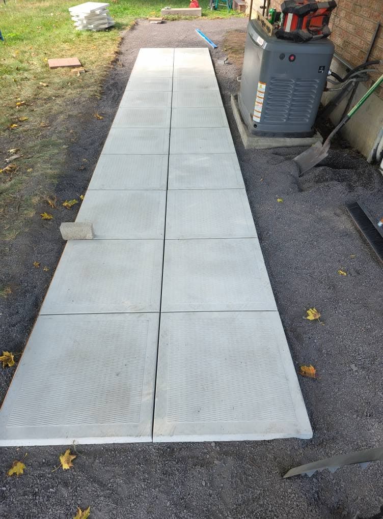 New precast slab walkway laid on fresh gravel beside a home generator
